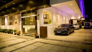 Una entrada de hotel moderna con un BMW estacionado frente, una escalera que conduce a la entrada y plantas en macetas a lo largo del camino.