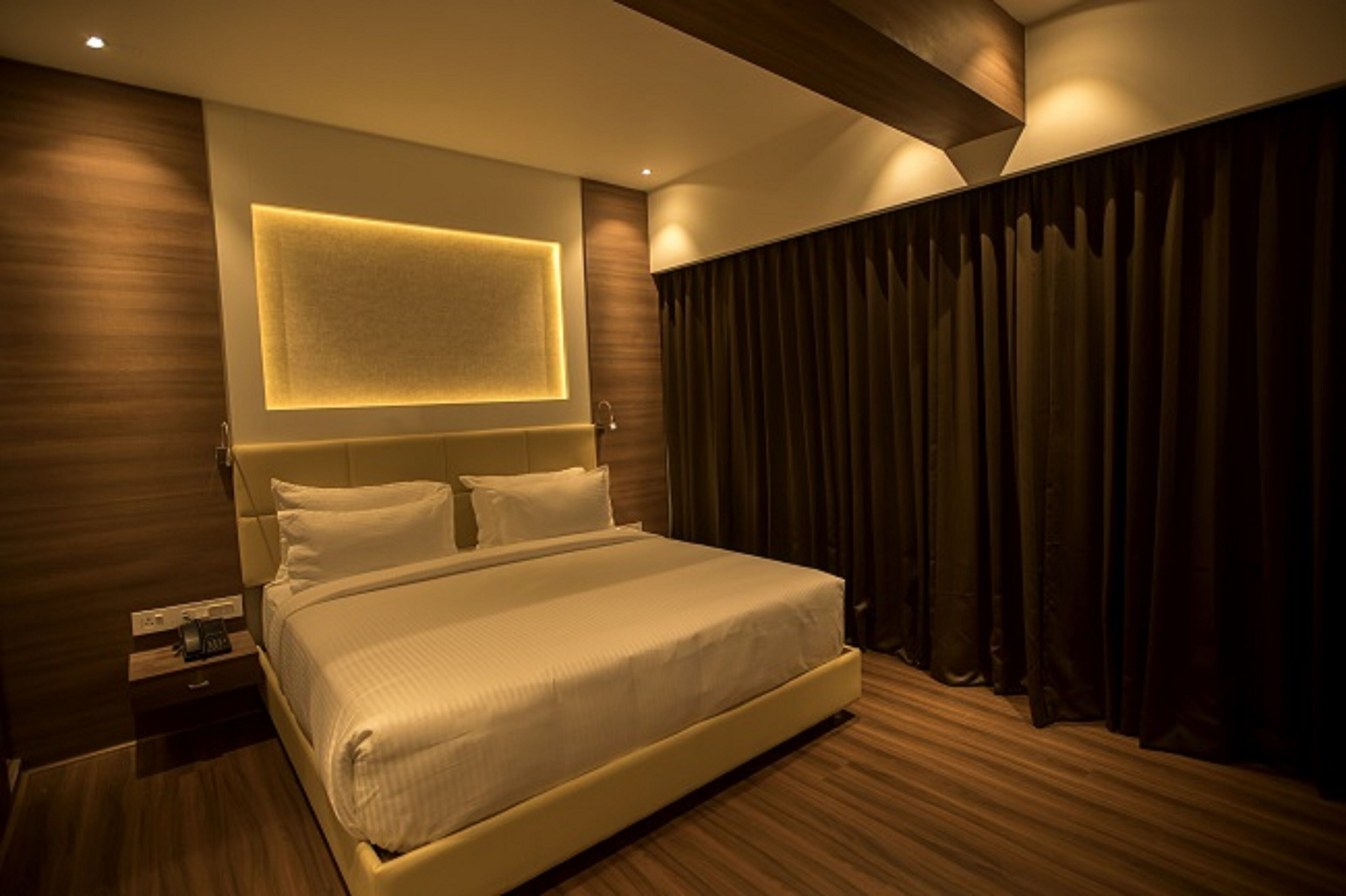 Una habitación de hotel moderna con una cama grande, una mesita de noche y una lámpara fijada a la pared.