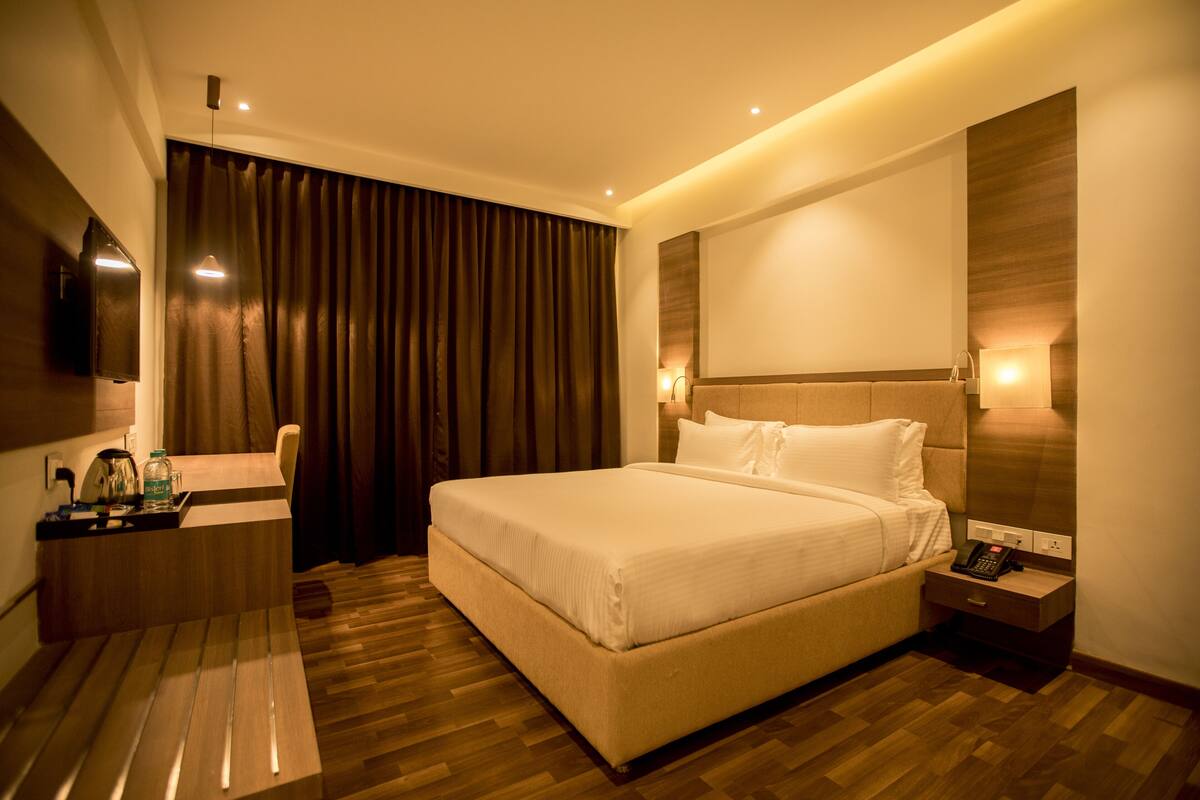 A hotel room with a large bed, bedside table, and a flat-screen TV mounted on the wall.