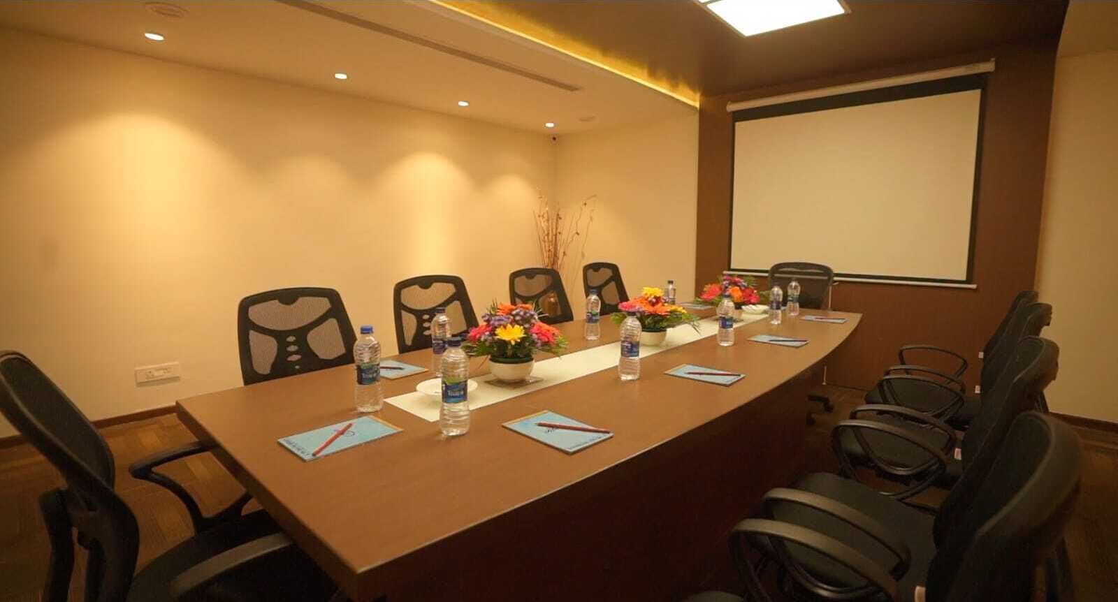 A conference room with a long table, chairs, water bottles, and a projector screen.
