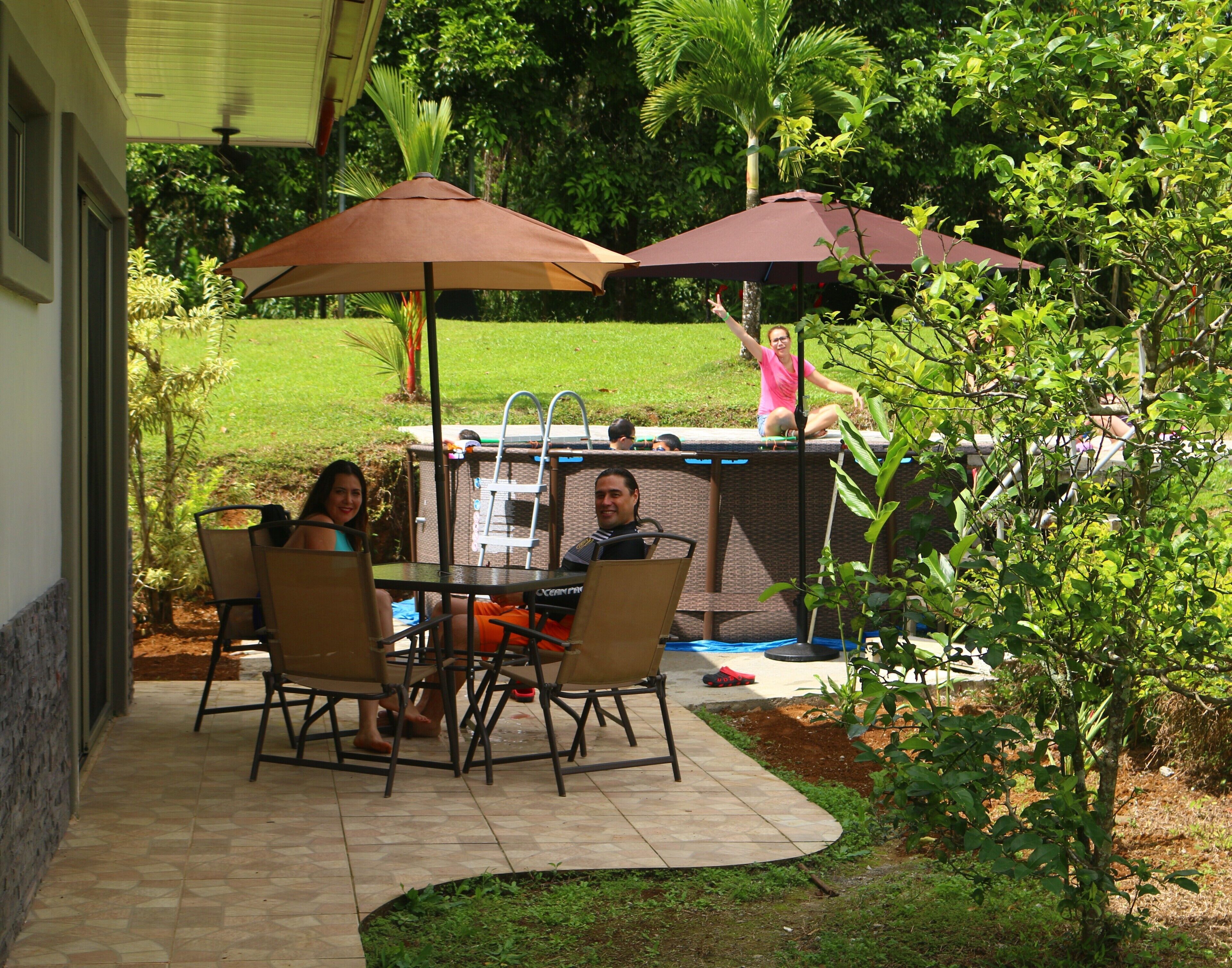 An outdoor patio with a table and chairs, two umbrellas, and a barbecue grill.