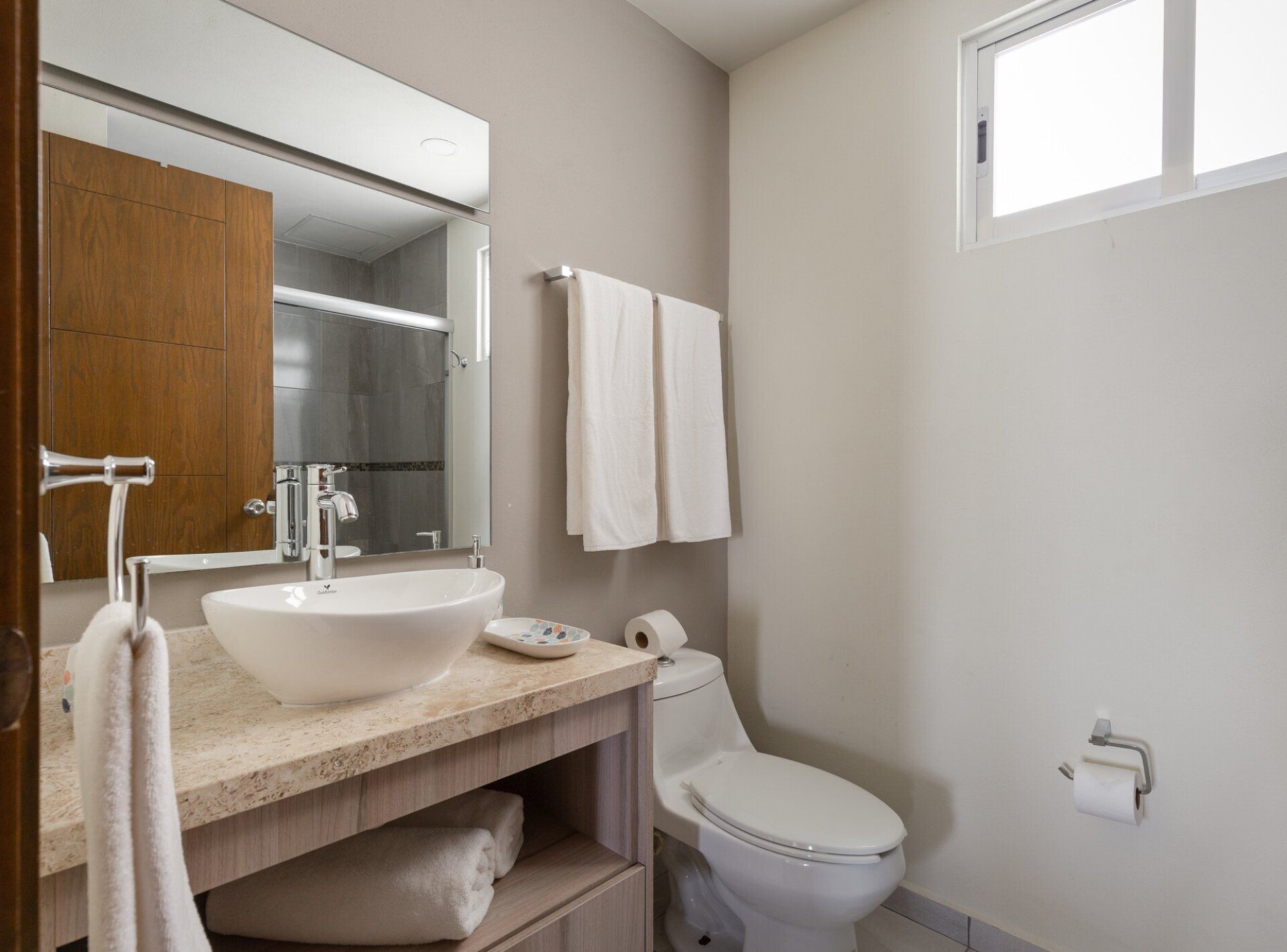 A modern bathroom with a large mirror, a sink, a toilet, and a window.