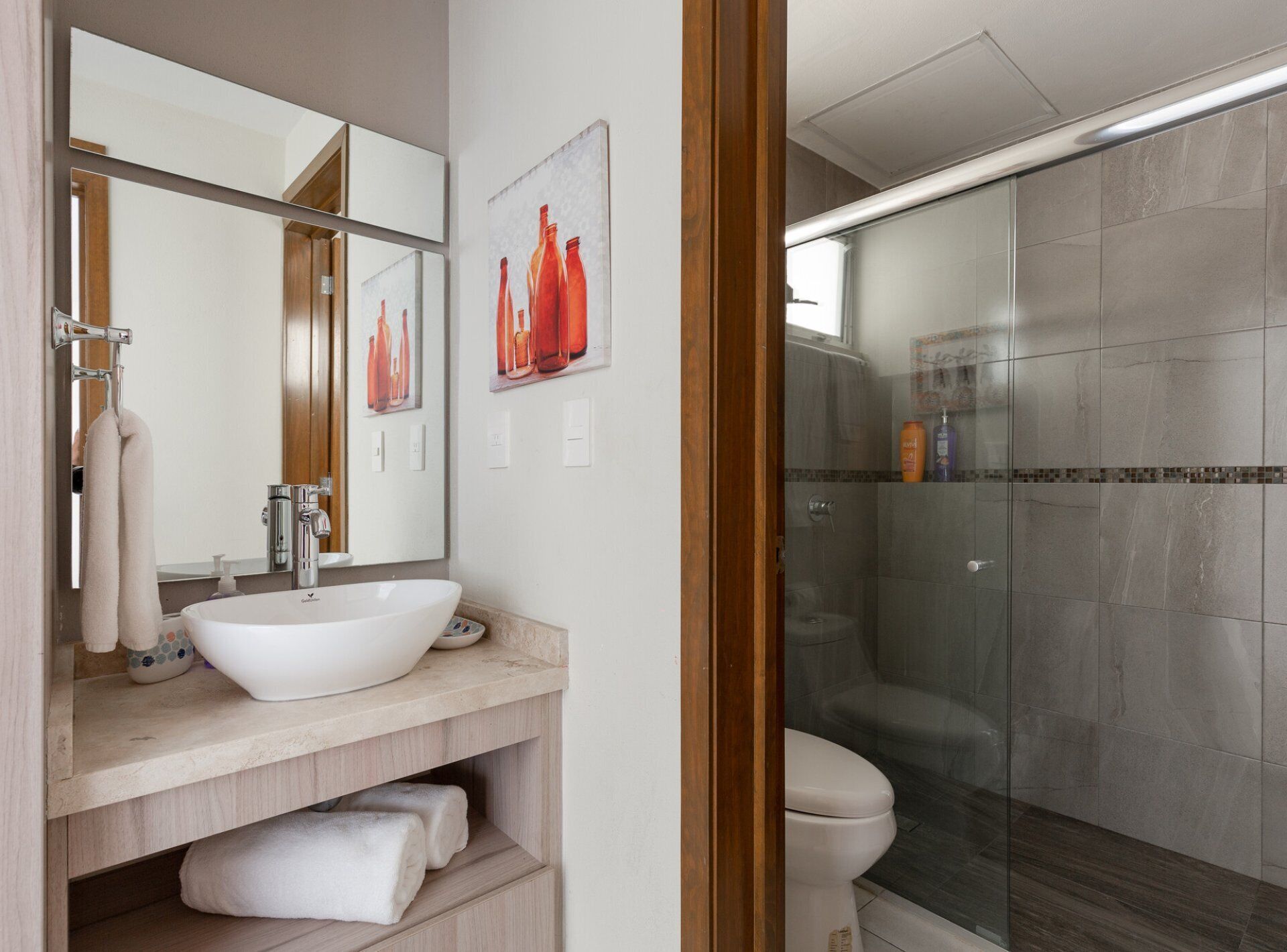 Un bagno moderno con uno specchio grande, un lavandino bianco, uno spazio doccia in vetro e un water.