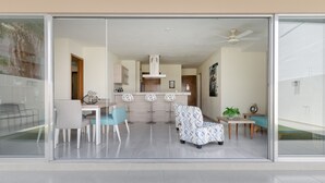 A modern living room with a glass partition, a dining area with a table and chairs, a kitchen with a central island, and a ceiling fan. - Large apartment with pool and terrace! (Cancún)