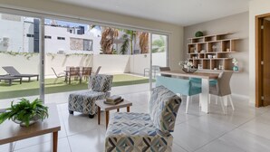 A modern living room with a dining area, large windows, and a view of the outside. - Large apartment with pool and terrace! (Cancún)