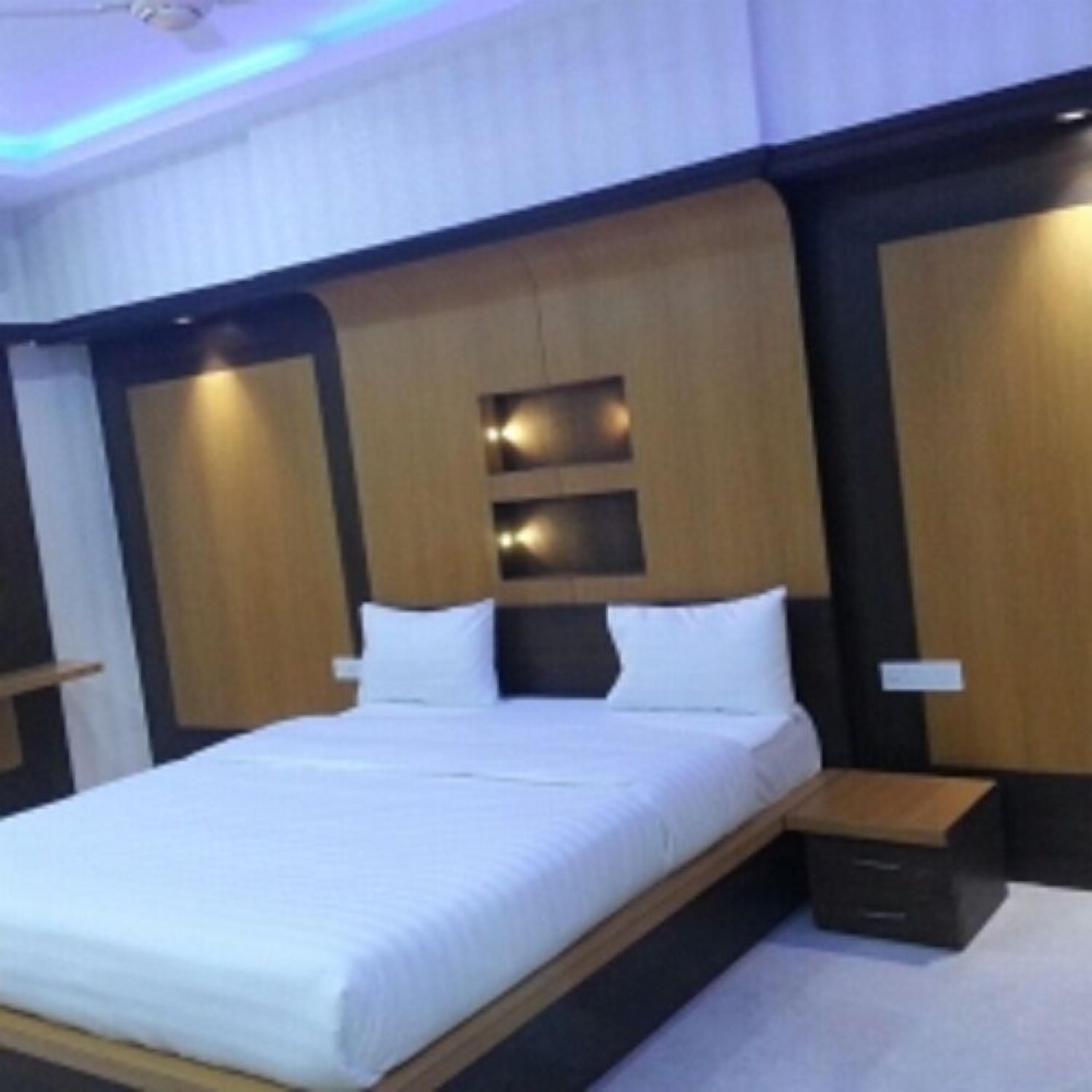 A modern hotel room with a large bed, a wooden headboard, and built-in lighting.