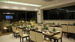 A restaurant with multiple tables and chairs, large windows, and a television screen.