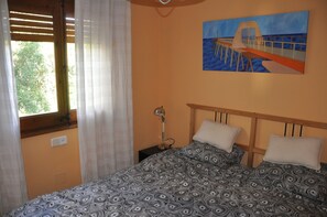 A bedroom with a bed, a nightstand, a lamp, a painting, and a window with curtains.