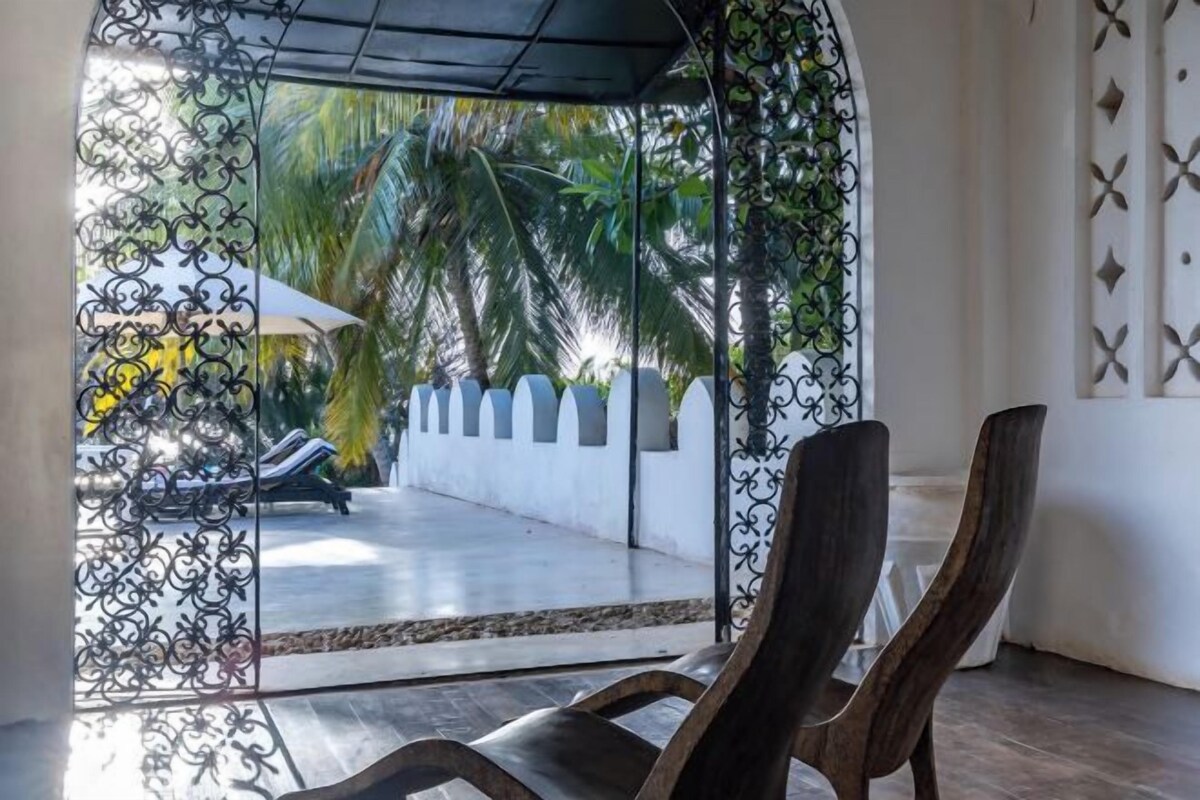 A room with a view of a pool area, featuring a chair and a decorative metal gate.