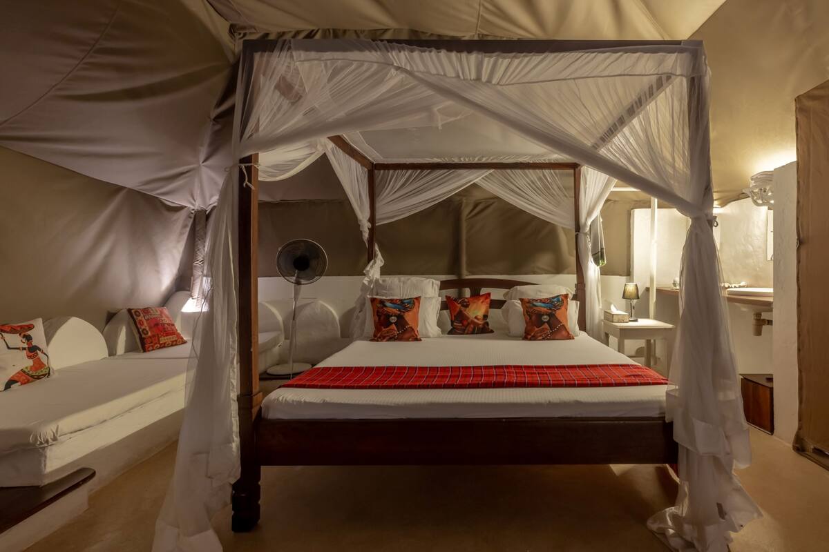 Una cama con dosel y cuatro columnas, con una colcha roja, ropa de cama blanca y almohadas de colores.