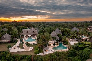 Ein Resort mit mehreren Pools, strohgedeckten Gebäuden und üppiger Vegetation.