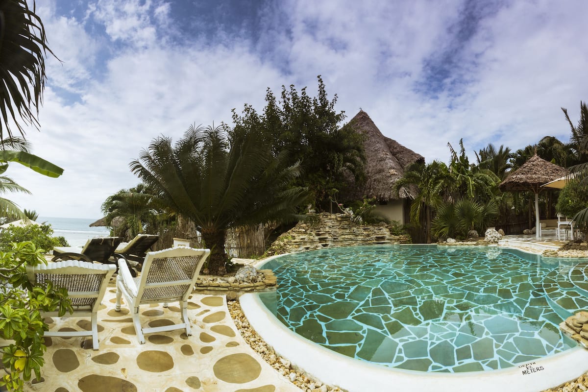 Un área de piscina con sillas de descanso, una estructura de techo de paja y vista al océano.