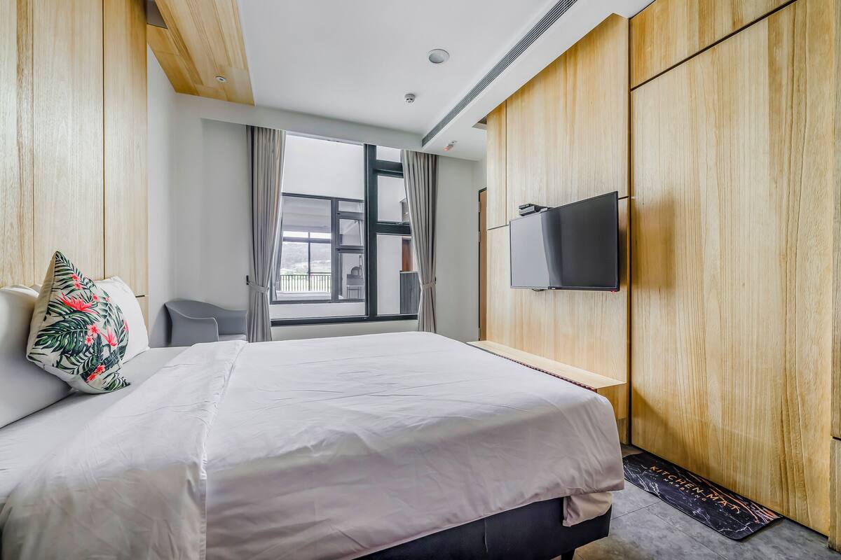 Habitació d'hotel amb un llit gran, un televisor fixat a la paret i una vista de l'exterior a través d'una finestra ampla.