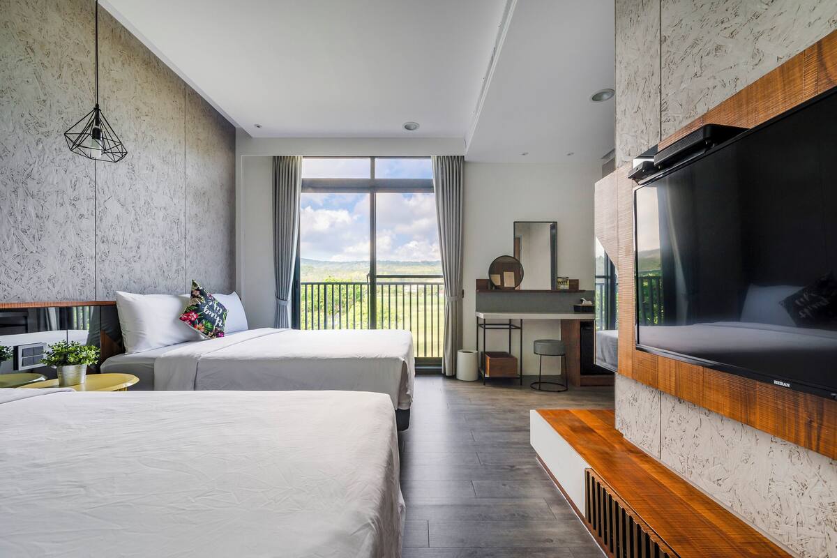 Habitació d'hotel moderna amb dos llits, un escriptori, televisió i un balcó amb vistes.