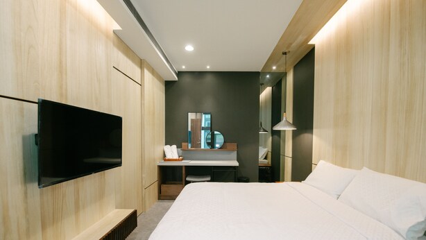 A modern hotel room with a large bed, a flat-screen TV mounted on the wall, a vanity with a mirror, and a desk with a lamp. - MH48 Hotel (Hengchun)