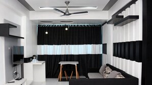 A modern, compact living space with a black and white color scheme, a ceiling fan, a flat-screen TV, a small table, and a sofa. - Shree Hotel (Danta)