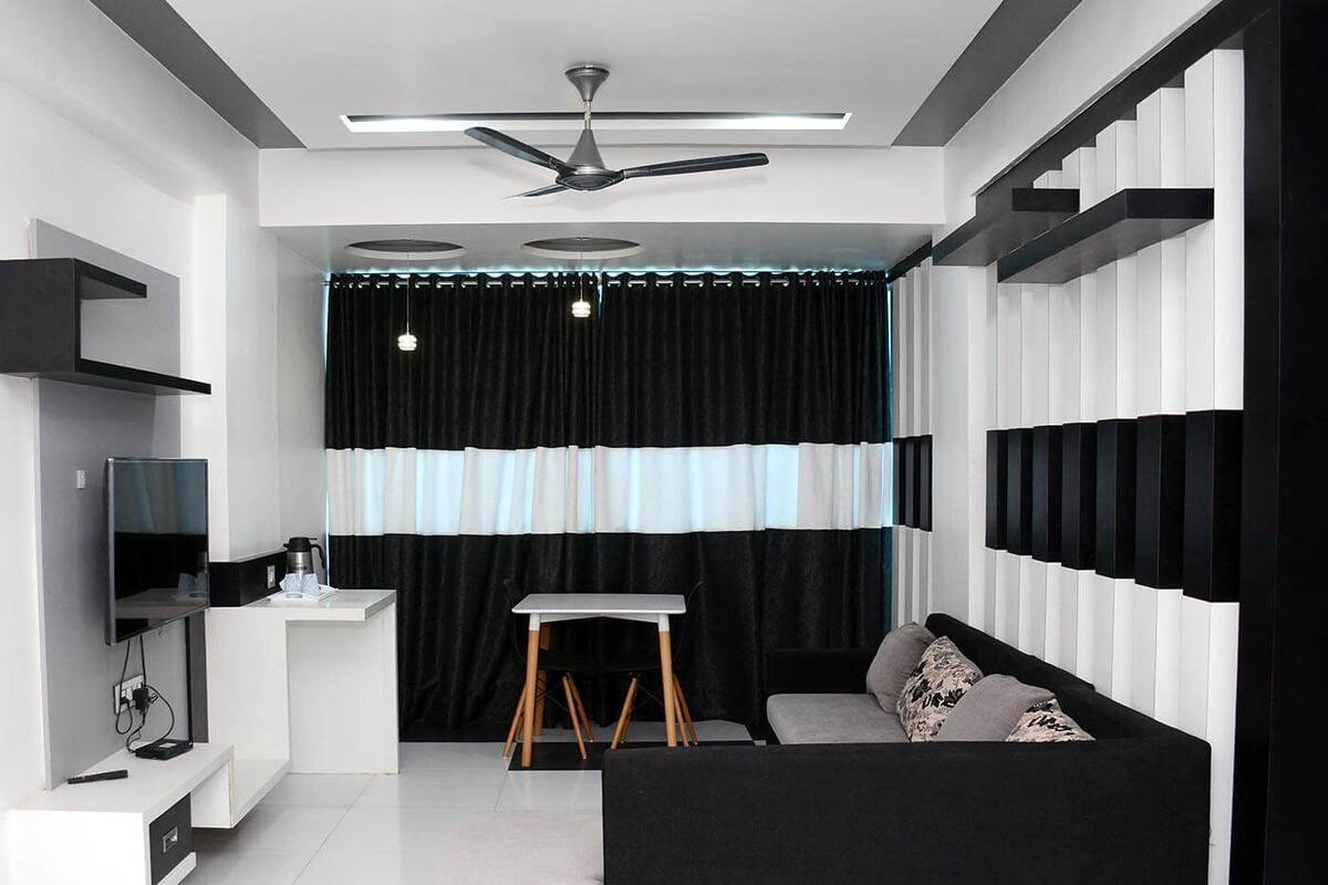 Ein modernes, kompaktes Wohnzimmer mit Schwarz-Weiß-Farbschema, Deckenventilator, Flachbildfernseher, kleinem Tisch und einer Couch.