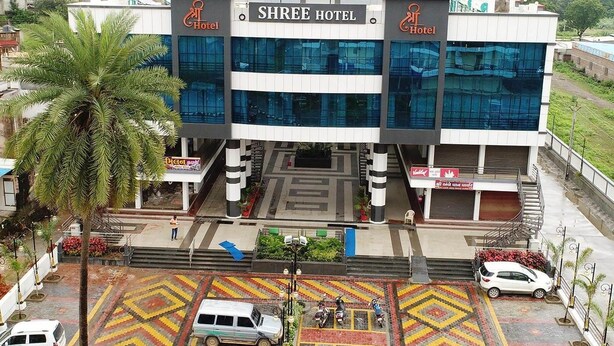 A modern hotel with a central entrance, multiple floors, and a parking area with a patterned ground. - Shree Hotel (Danta)
