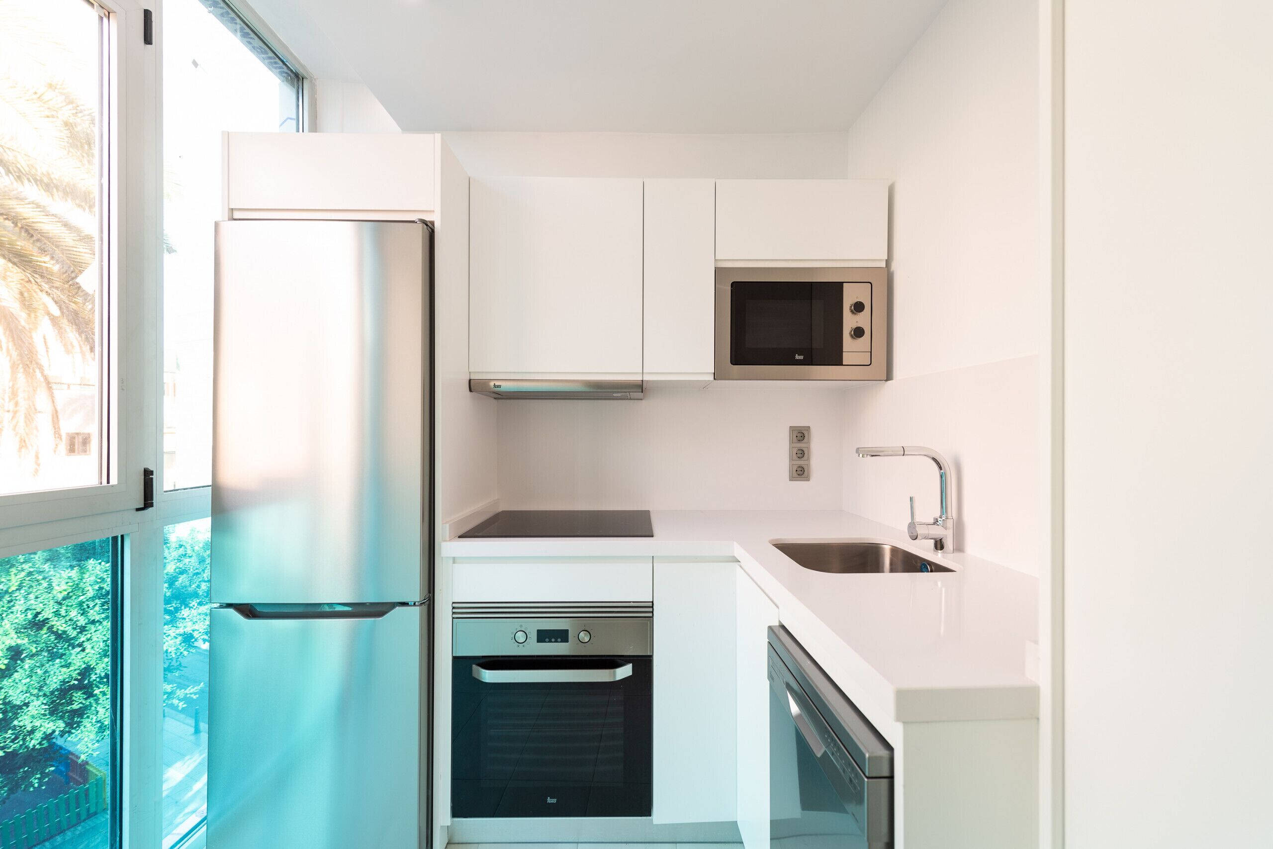 A modern kitchen with white cabinetry, a stainless steel refrigerator, a microwave, a dishwasher, and a built-in oven.