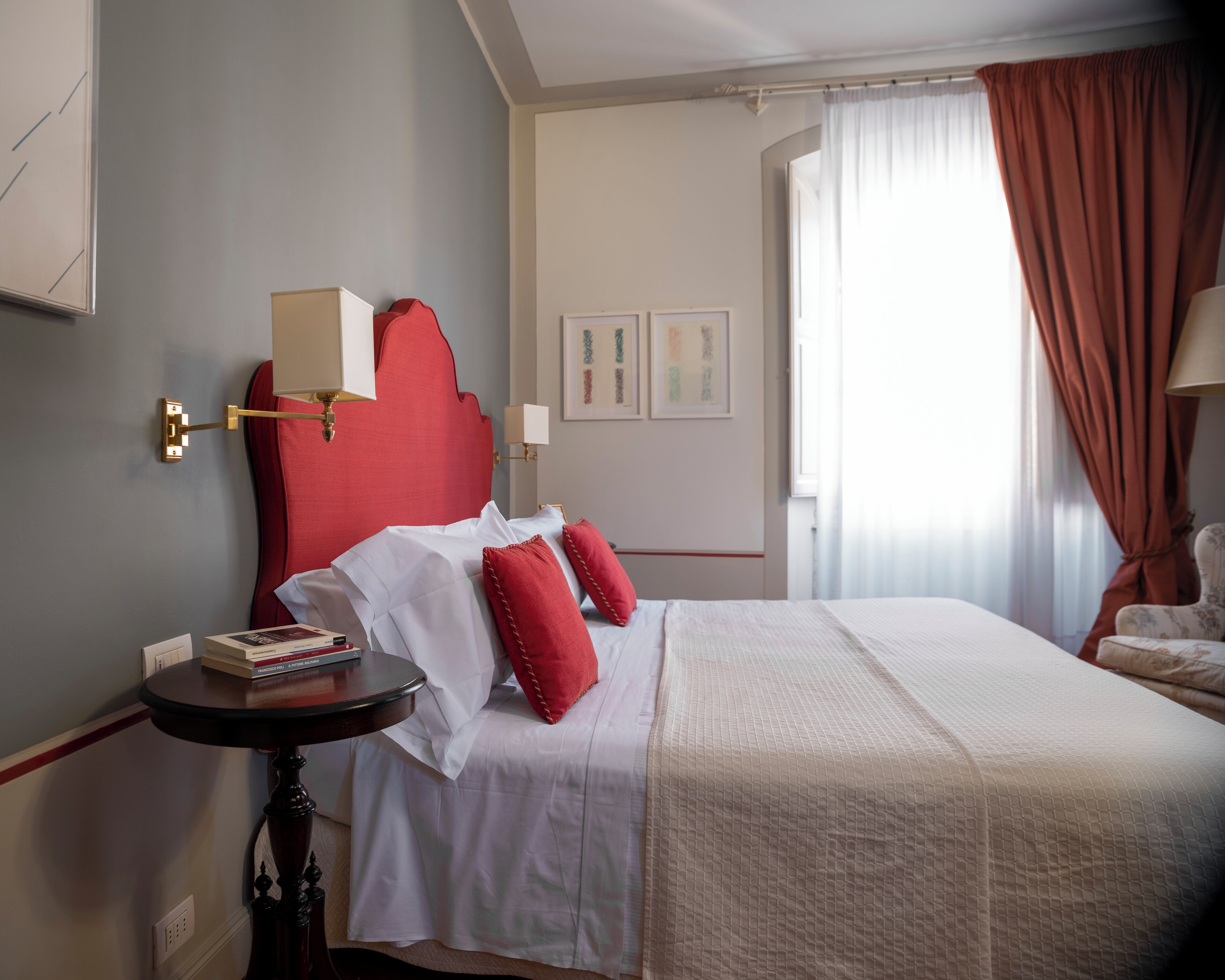 Una habitación de hotel con una cama, una mesita de noche, una lámpara y una ventana con cortinas.