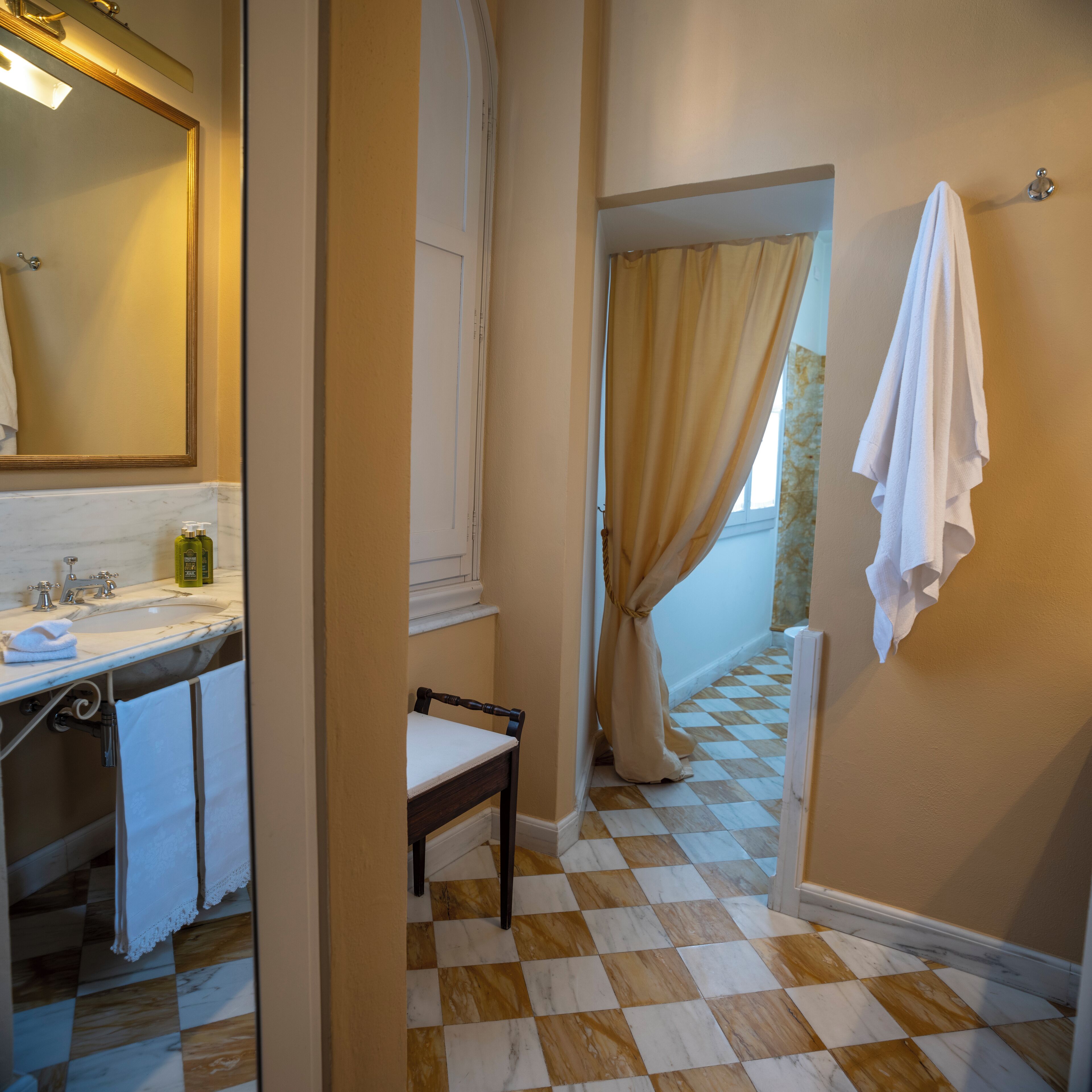 A bathroom with a checkered floor, a sink with a mirror, and a chair.