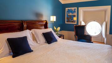 A hotel room with a large bed, a round window, and a blue wall.