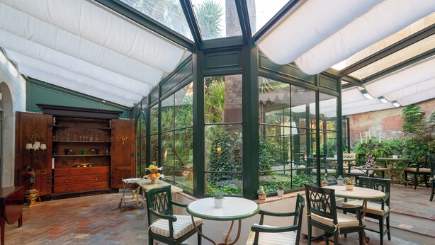 A conservatory with a glass ceiling, wooden furniture, and a view of the garden. - Albergo Pietrasanta (Pietrasanta)