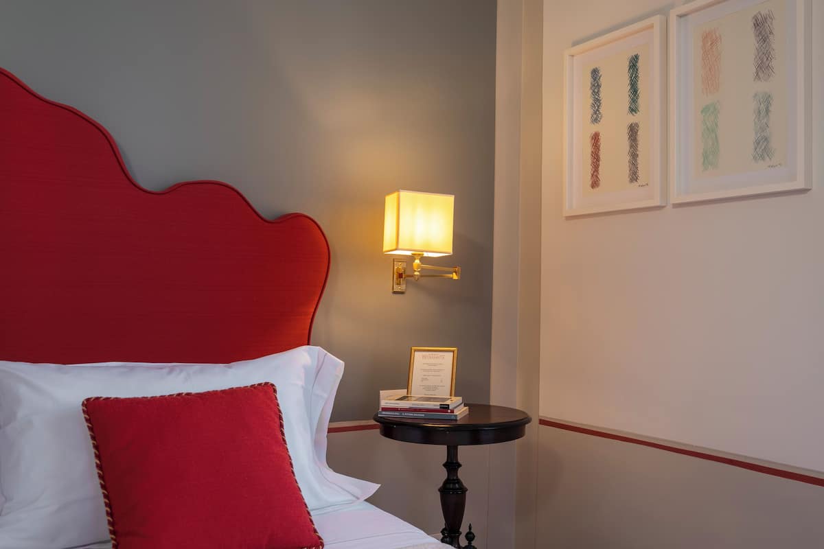 A neatly made bed with a red headboard, a bedside table with a lamp, and framed artwork on the wall.