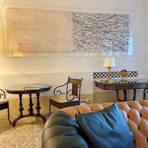 Una habitación con una mesa redonda, una silla acolchada, una lámpara y un cuadro abstracto grande en la pared.
