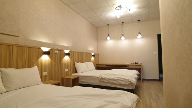 A hotel room with two beds, wooden headboards, bedside tables, and pendant lights. - Duo Yuan Hua BB (Chaozhou)