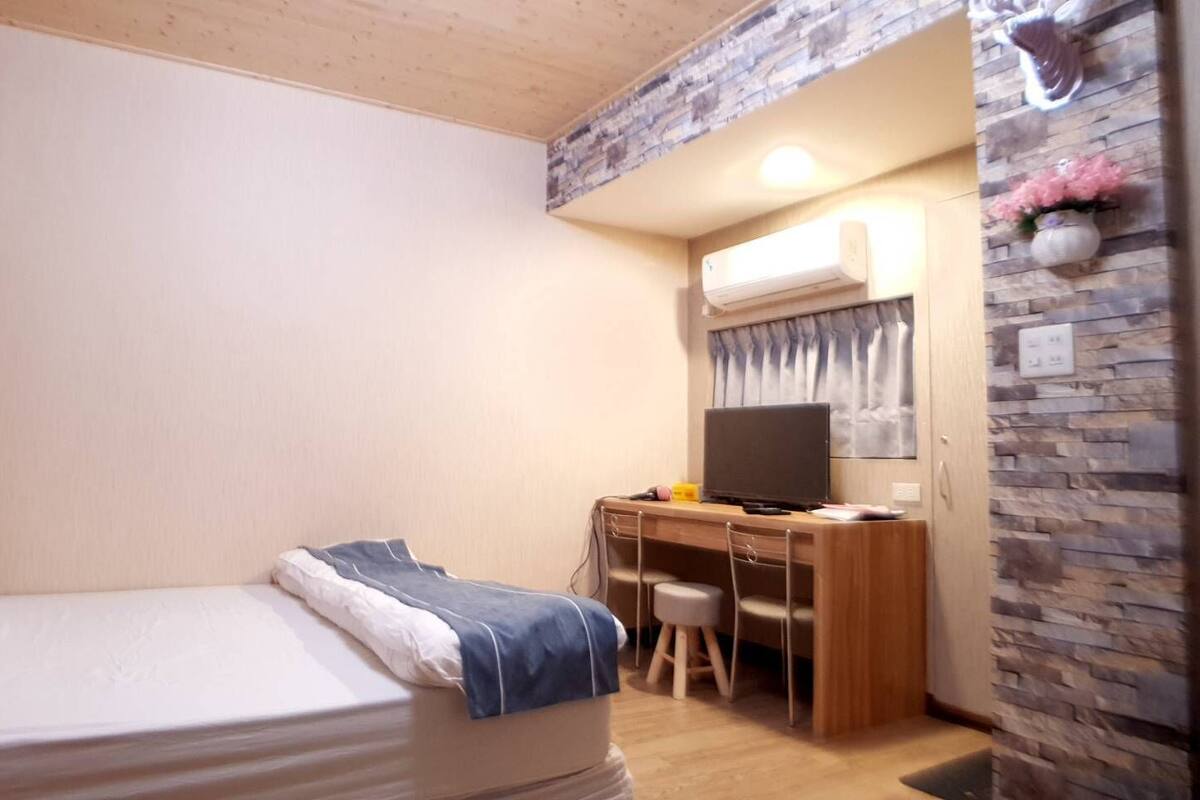 Une chambre à coucher avec un lit, un bureau avec un ordinateur et une télévision.