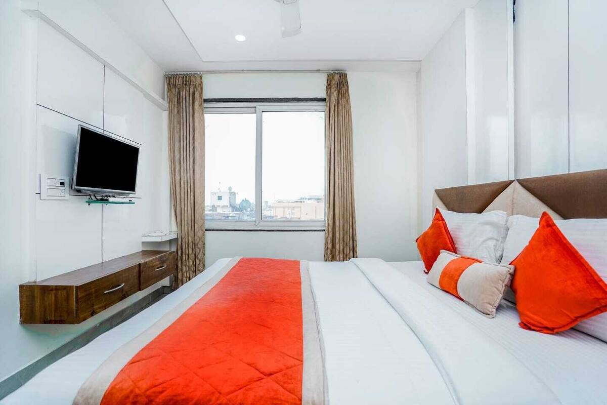 Quarto de hotel moderno com uma cama grande, televisão de tela plana na parede e vista para a cidade pela janela.