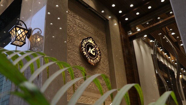 A building entrance with a decorative wall, a sign with 'AG' logo, and a staircase.