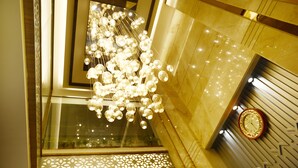 A modern interior with a decorative chandelier, a wall-mounted clock, and a patterned window design.