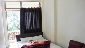 A room with a bed, a red chair, and a window with curtains. - Hotel Banjara (Pipariya)