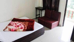 A bedroom with a bed, a red sofa, a small table, and a window with curtains. - Hotel Banjara (Pipariya)