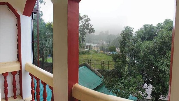 A balcony with a view of a green landscape and a building in the distance. - Hotel Banjara (Pipariya)