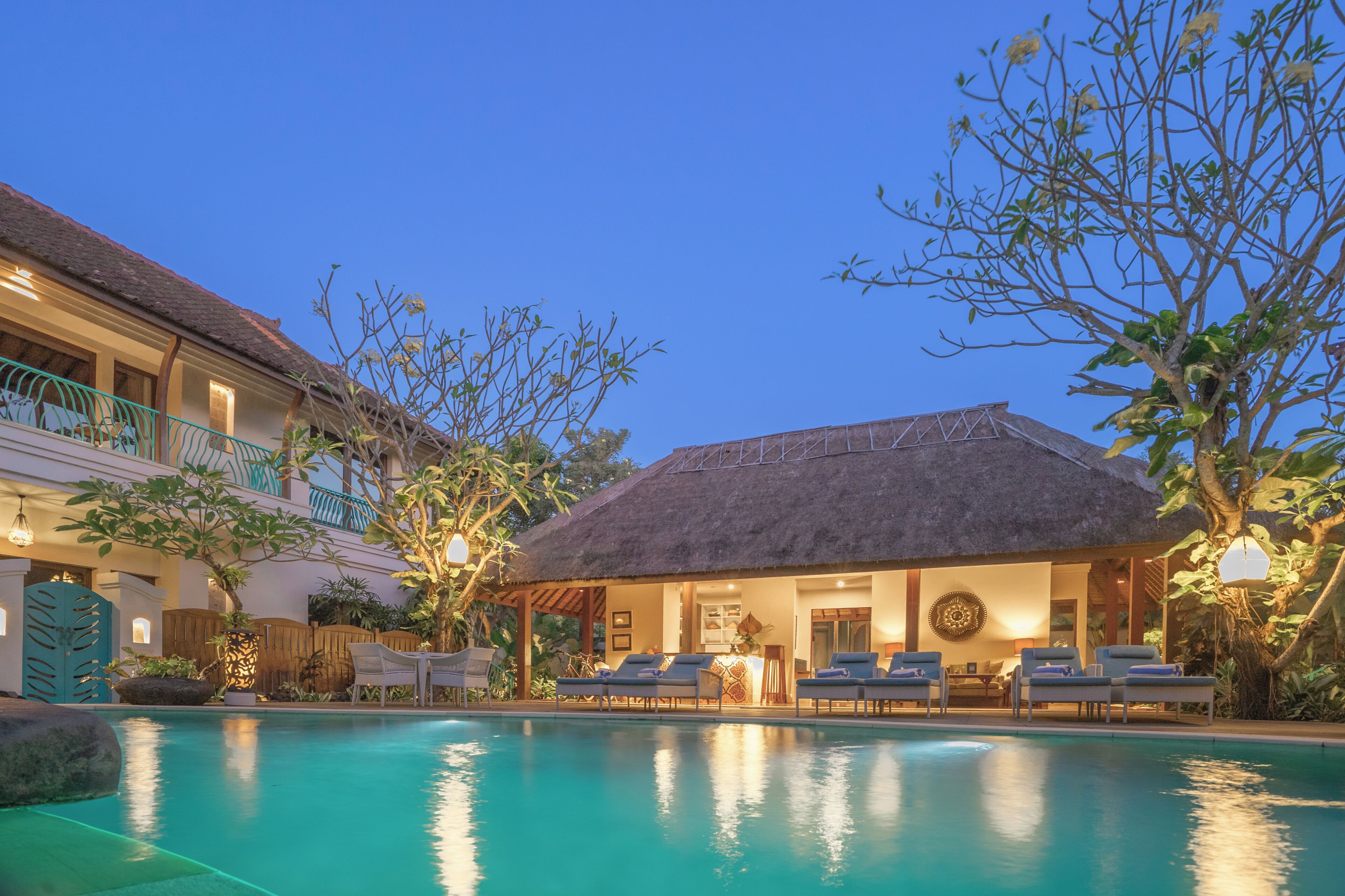 A poolside area with lounge chairs, a thatched-roof structure, and a building with balconies.