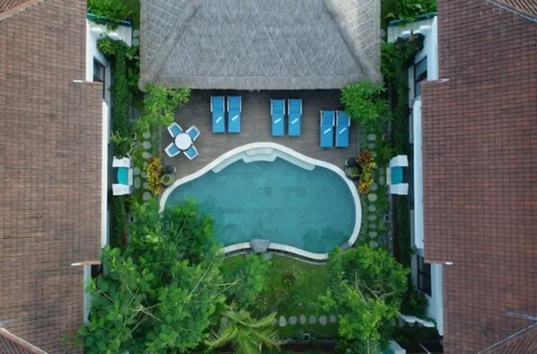 An aerial view of a swimming pool surrounded by lounge chairs and umbrellas, with a thatched roof structure above.