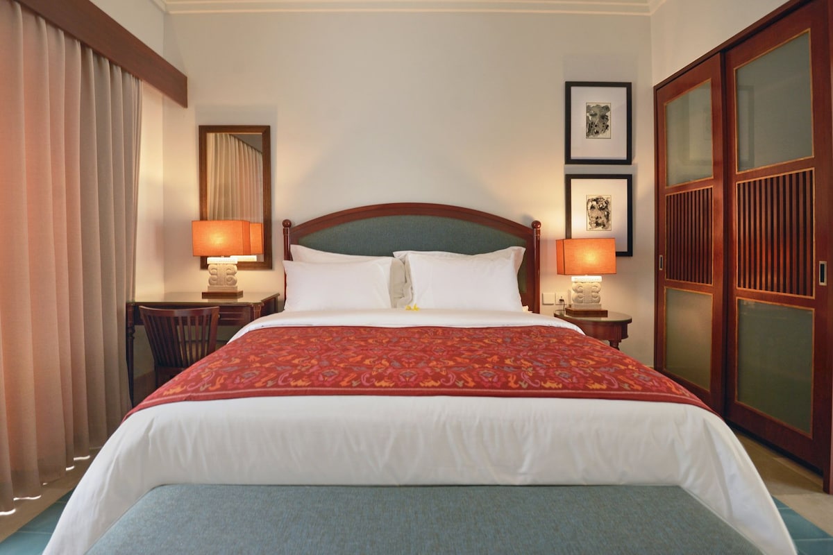A hotel room with a large bed, two bedside lamps, a desk with a chair, and a wardrobe.