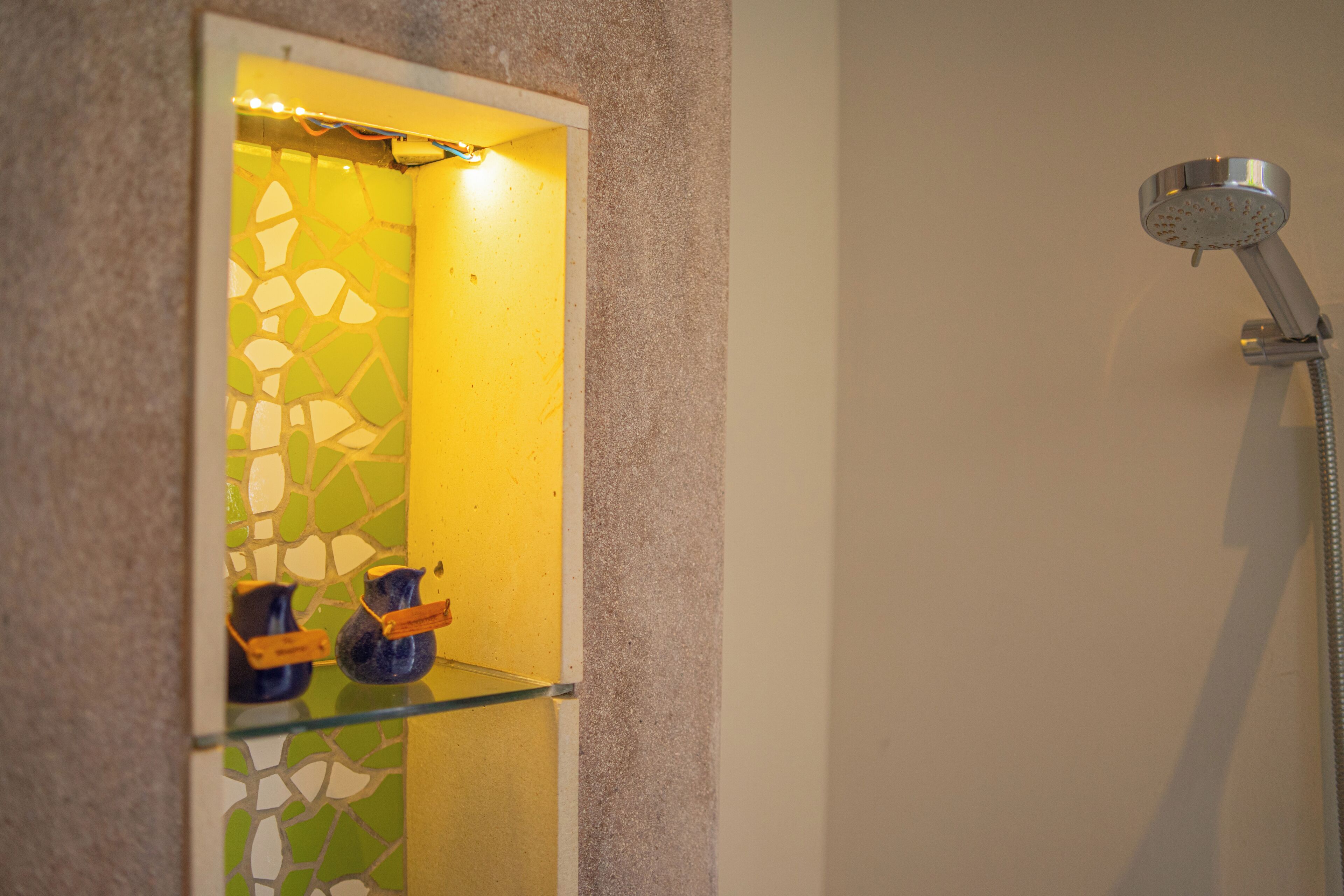 Un baño con pared amarilla, cabezal de ducha y espejo que refleja un reverso de mosaicos.