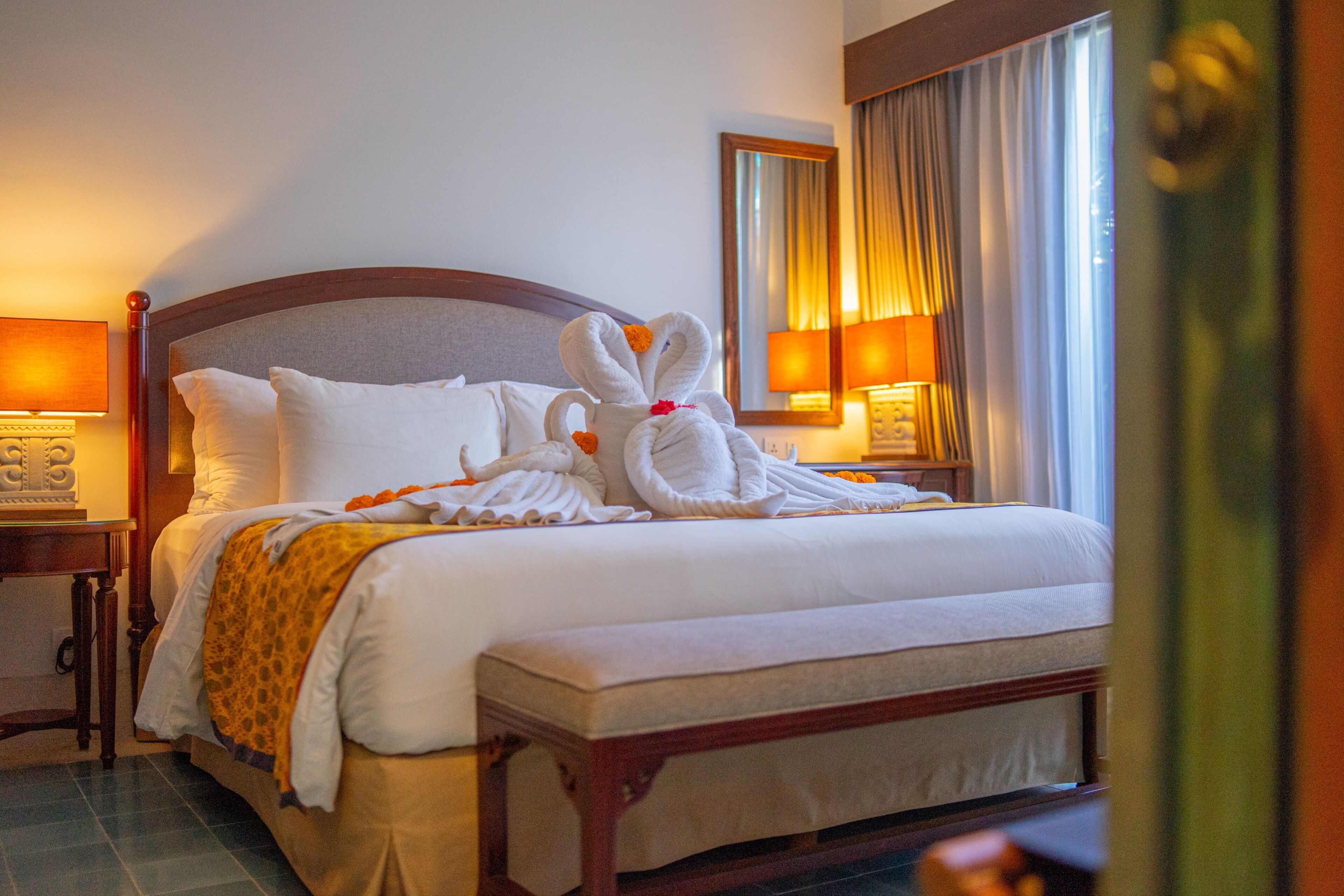 A hotel room with a neatly made bed, a bedside table with a lamp, and a large window with curtains.