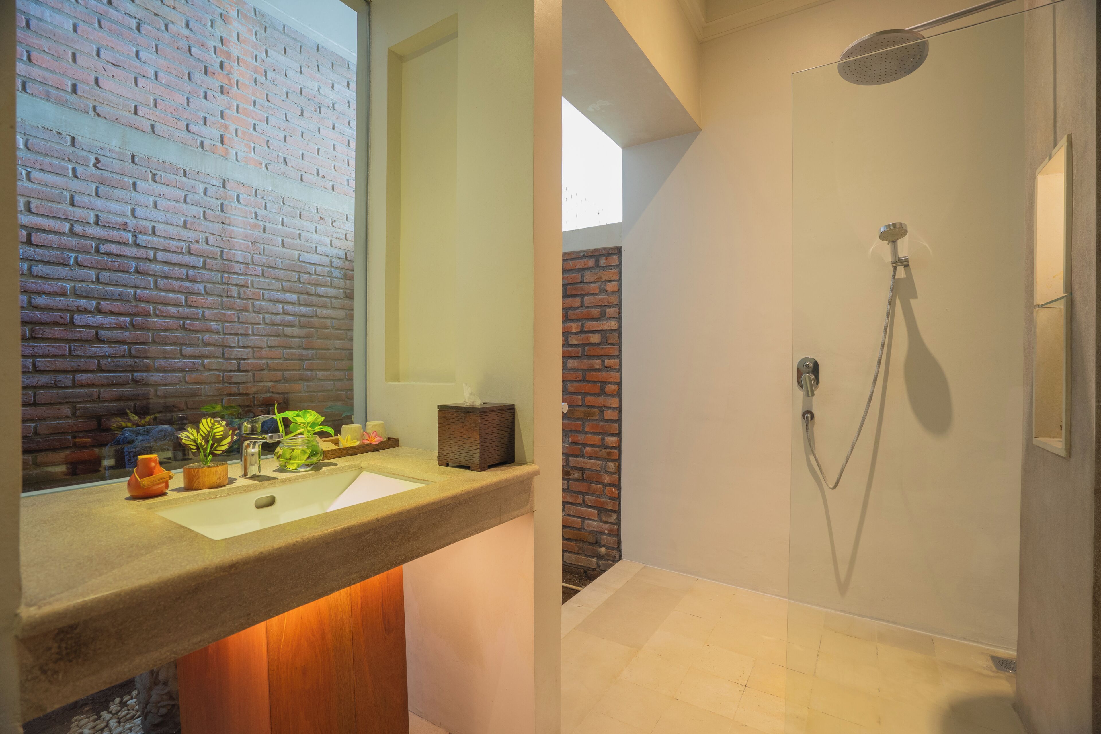 A bathroom with a brick wall, a sink with decorative items, and a shower with a handheld showerhead.