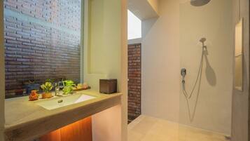 A bathroom with a brick wall, a sink with decorative items, and a shower with a handheld showerhead.