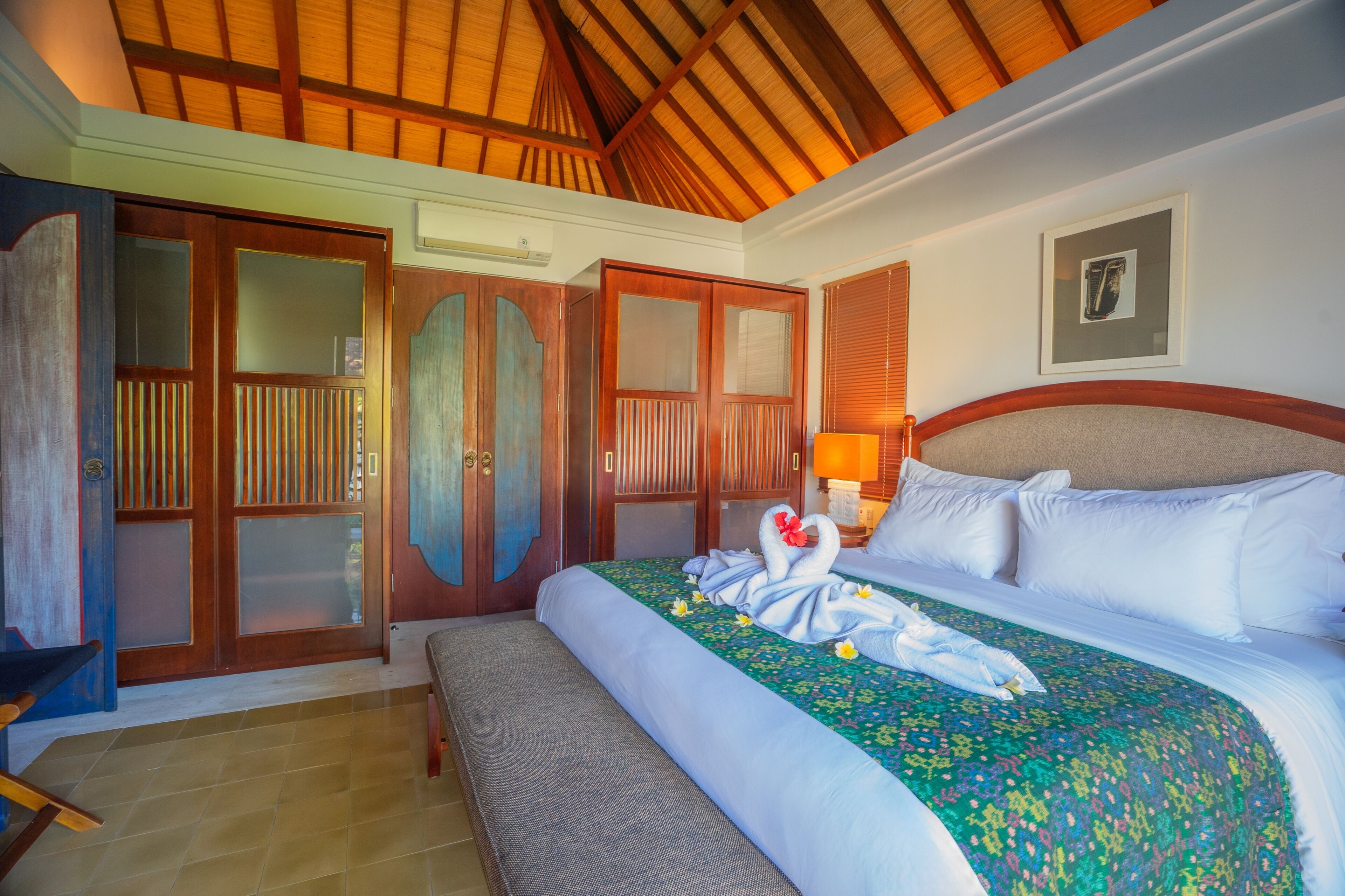 Quarto de hotel com cama, um banco, guarda-roupa e teto com vigas de madeira.