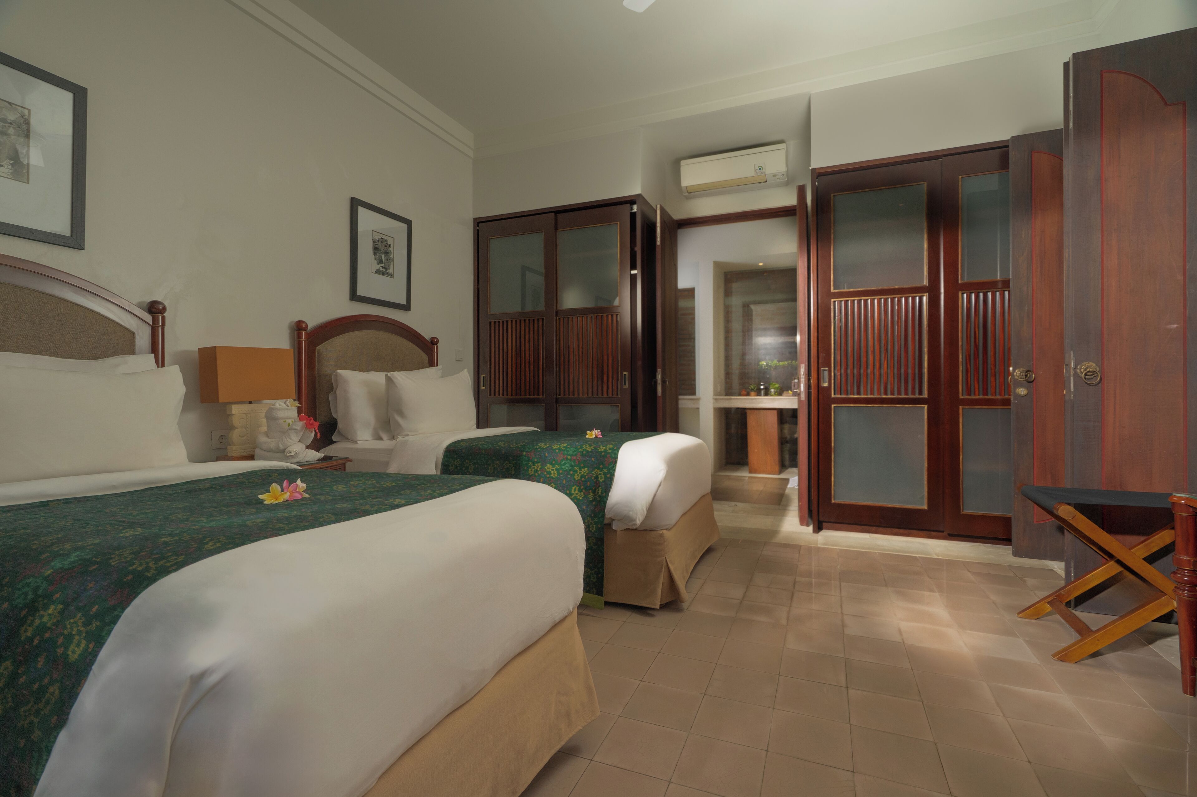 A hotel room with two beds, a wardrobe, a desk, and an air conditioning unit.