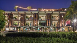 Un hotel de varios pisos con un diseño arquitectónico moderno, que cuenta con balcones con plantas, un área de piscina y un espacio exterior bien iluminado.