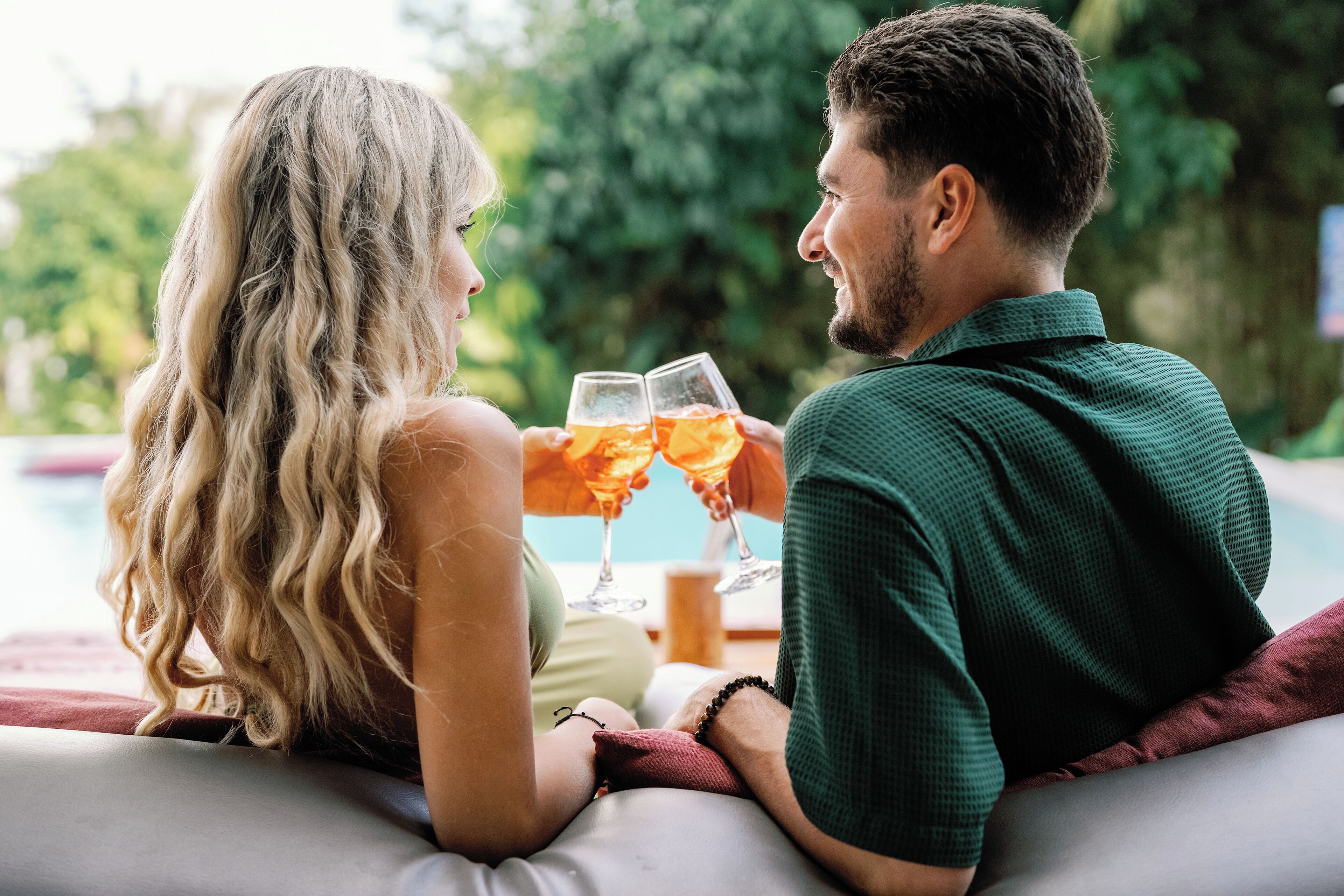 A couple sitting by a poolside with drinks, surrounded by greenery.
