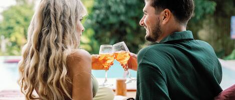 A couple sitting by a poolside with drinks, surrounded by greenery.