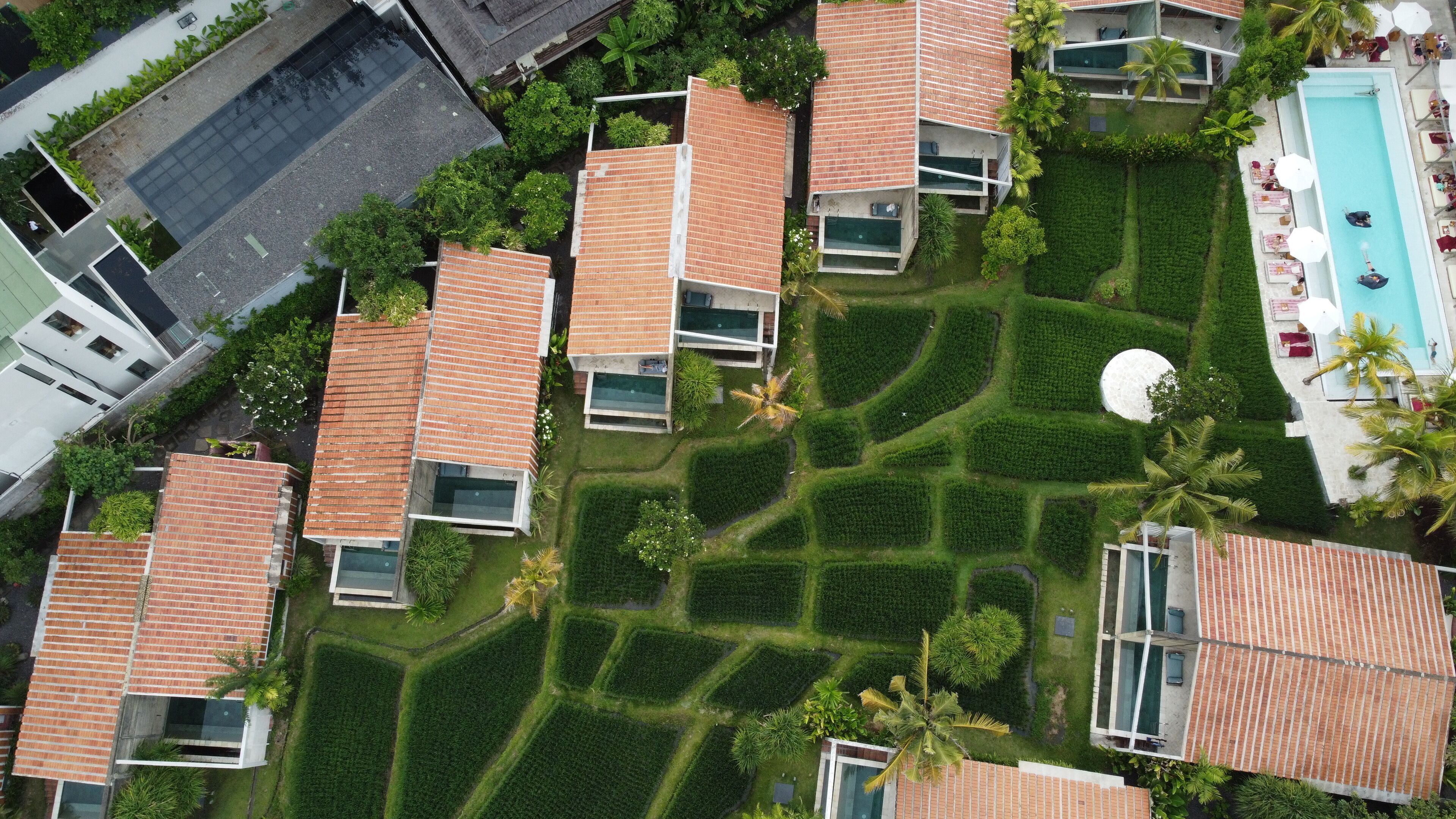 Luchtbeeld van een woongebied met moderne huizen, een zwembad en verzorgde tuinen.